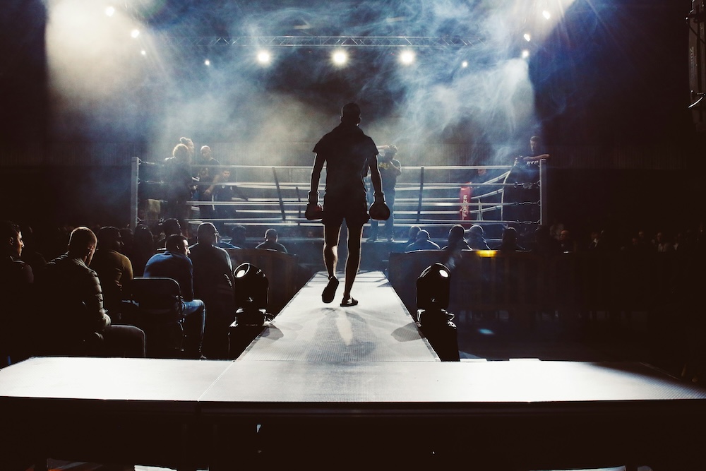 A silhouette of a boxer walking to a boxing ring with an audience either side of him to symbolise the showdown: CNC machining vs 3D printing.